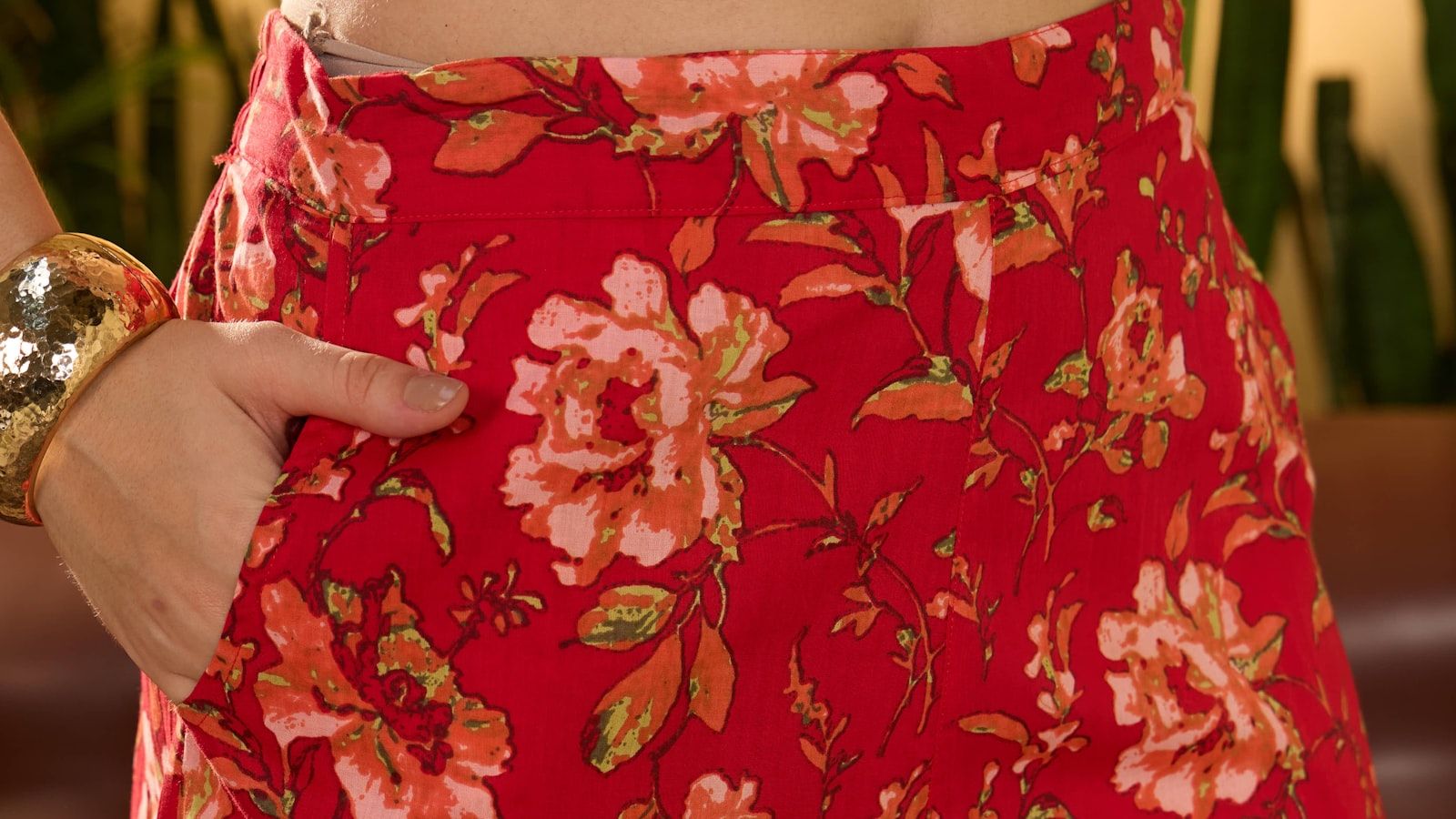 Close-up of a red floral print lounge pant showing the waistband seam and a hand in the side-seam pocket