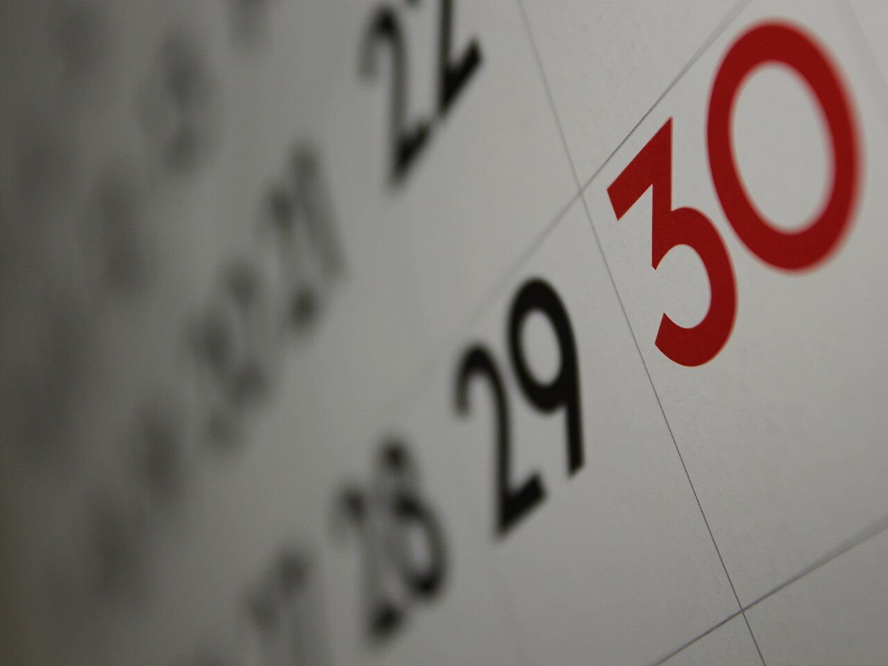 Close-up of a wall calendar grid with the 30th printed in red beside black weekday dates