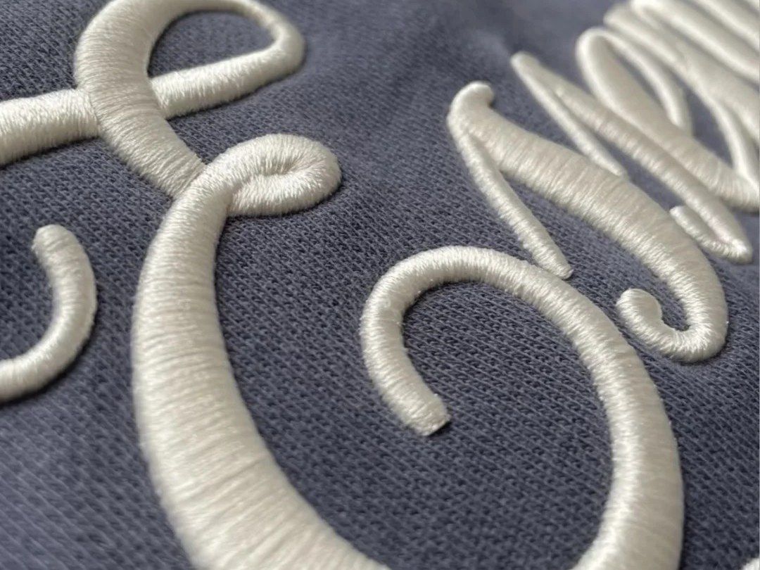 Close-up of raised cream script embroidery on grey knit fabric