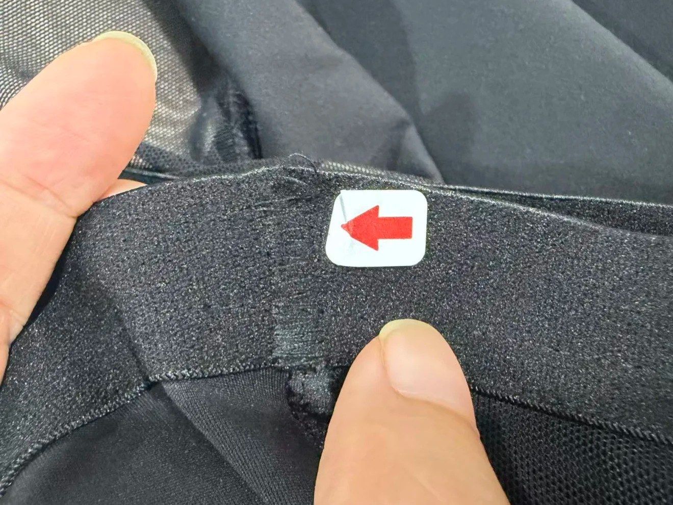 Inspector holding a garment waistband marked with a red arrow sticker at a stitching defect