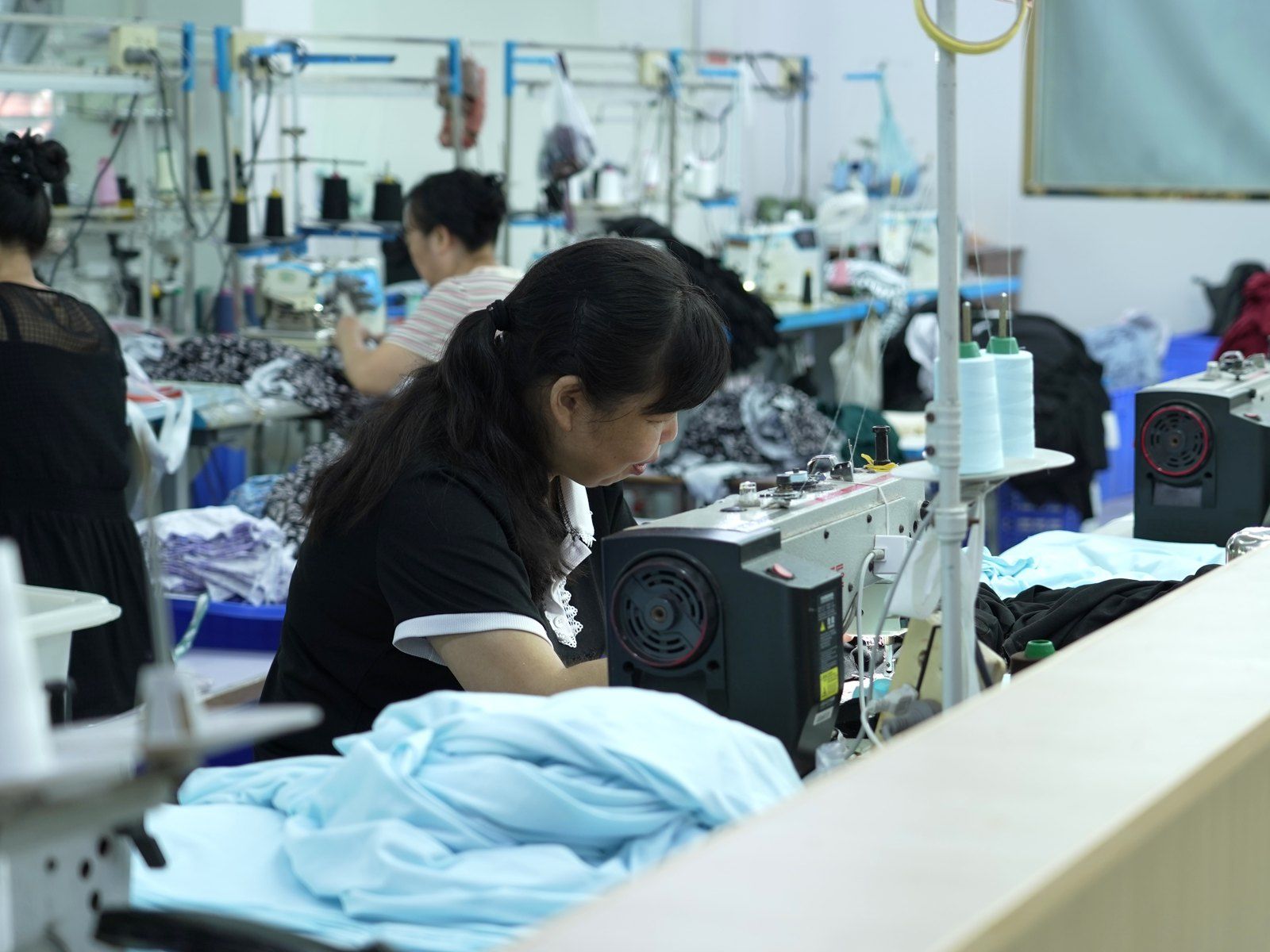 Sewing operator at her machine on our production floor, with light blue fabric in the foreground
