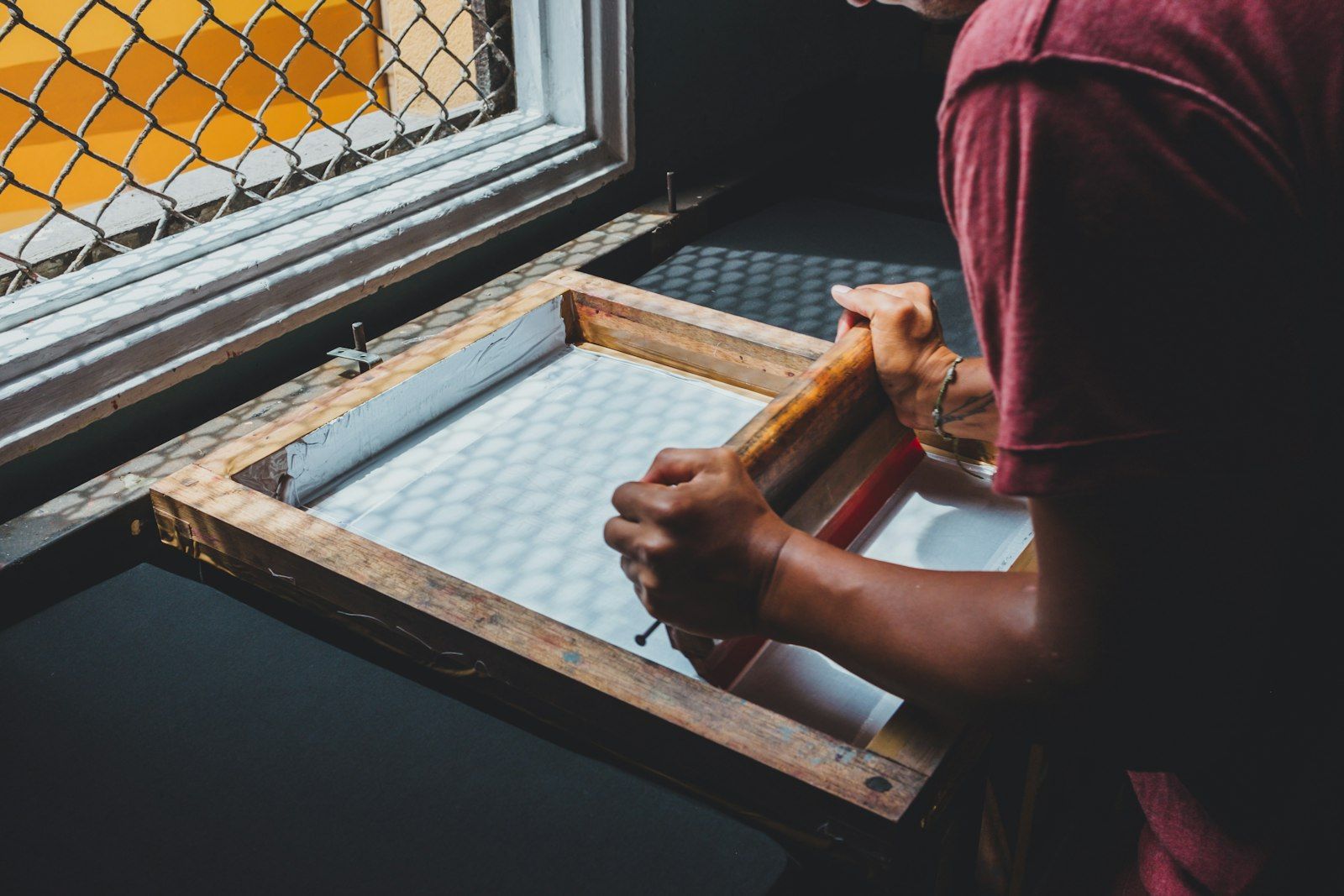 Print worker holding a blank screen-printing frame at a workshop window before artwork is exposed onto it