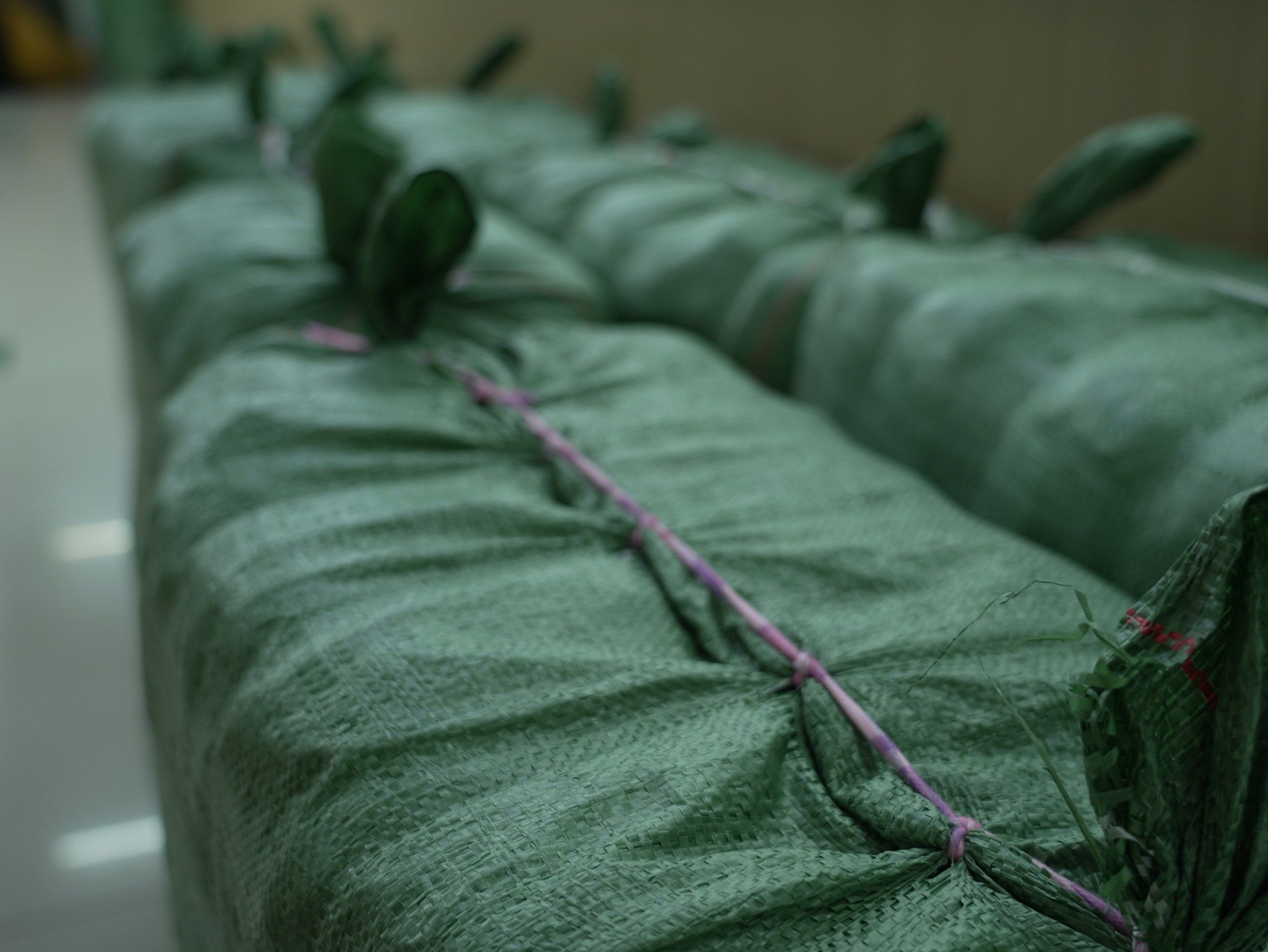 Rows of green woven sacks of finished garments, tied with pink cord, lined up in our final inspection area