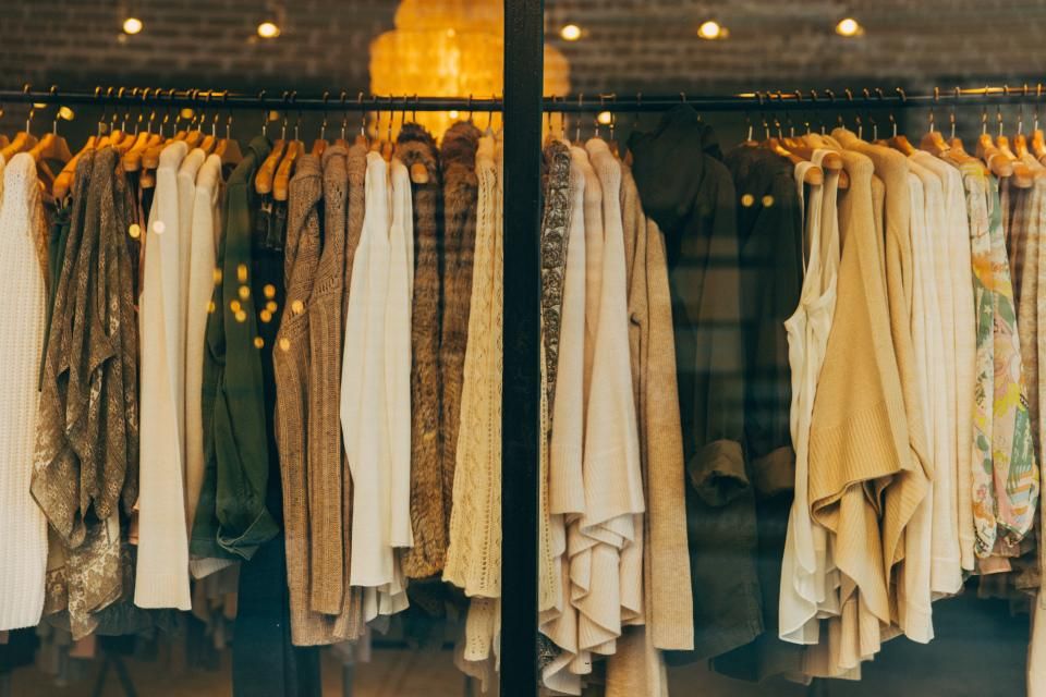Two rails of neutral-toned knit cardigans and sweaters hanging on wooden hangers behind a shop window