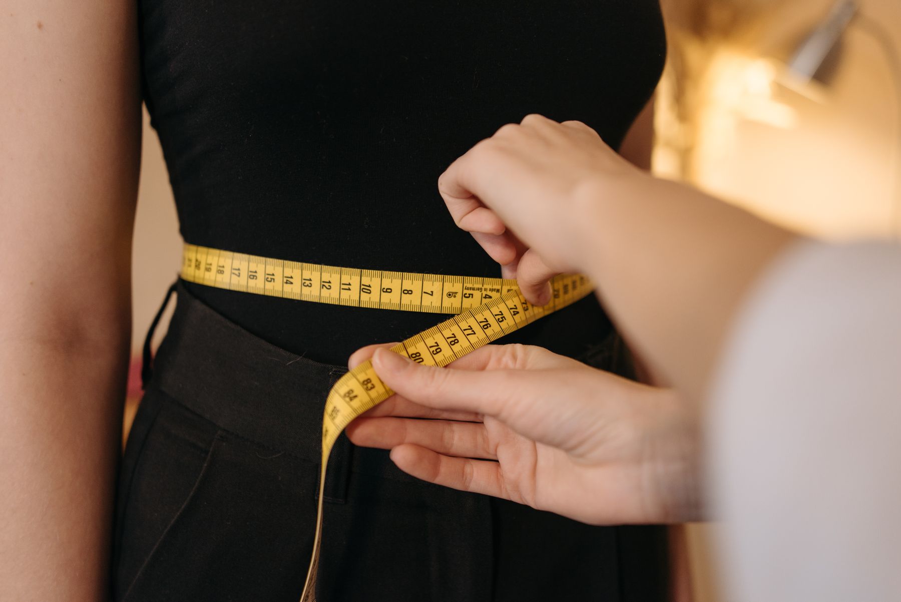 Tailor measuring a waist with a yellow tape measure during a garment fitting
