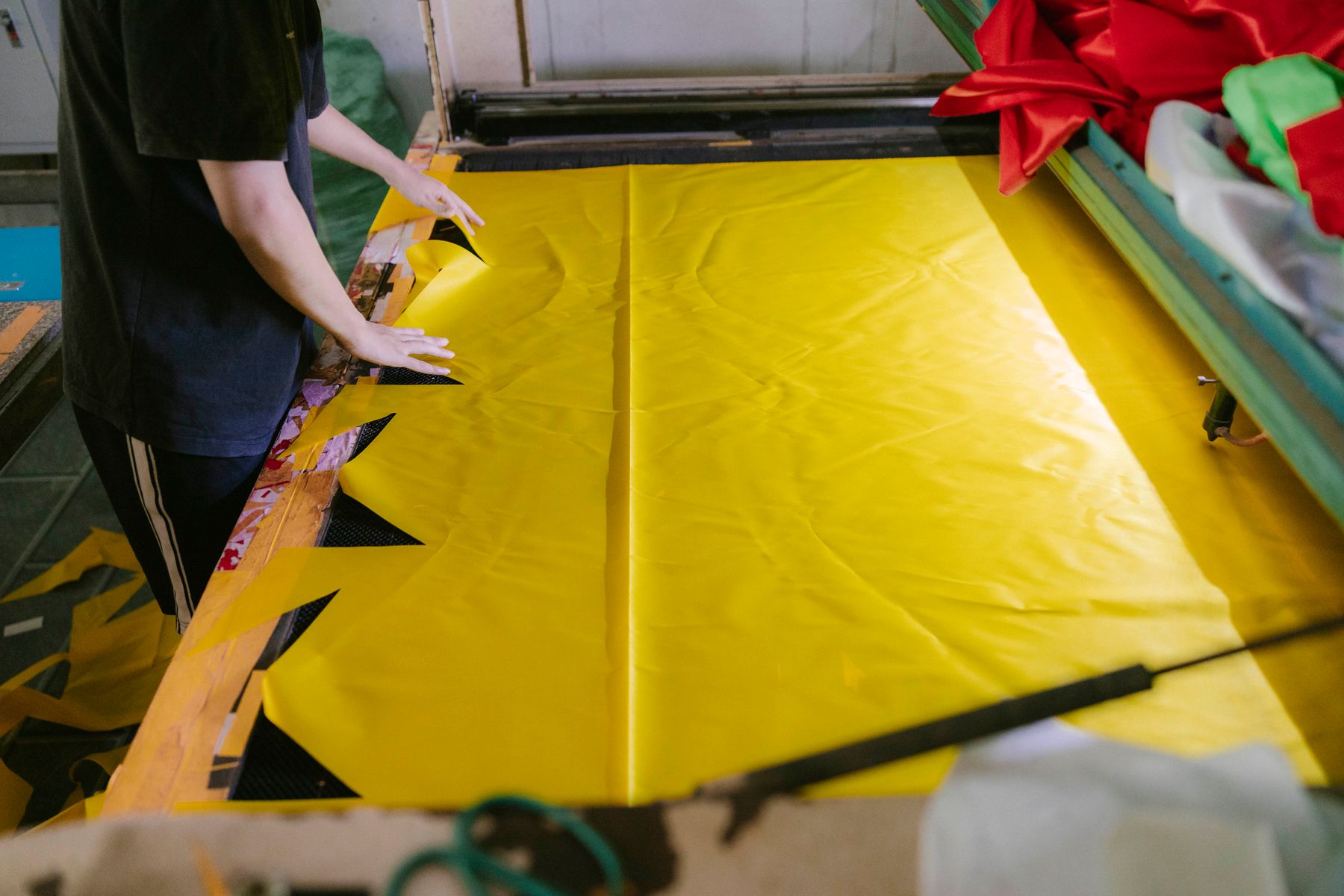 Worker spreading a length of yellow fabric across a factory cutting table