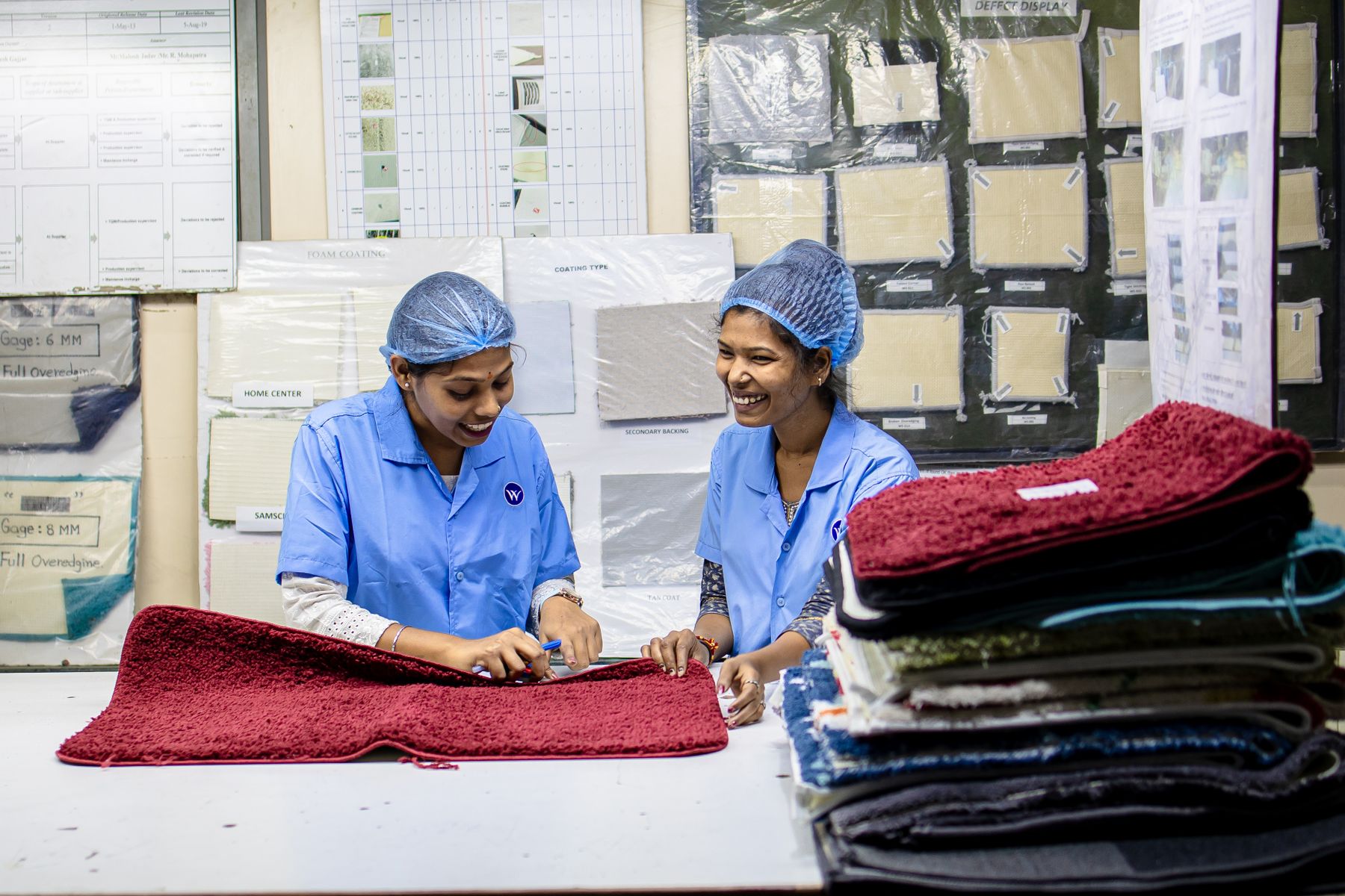 Two textile workers inspecting fabric beside a wall of approved swatches