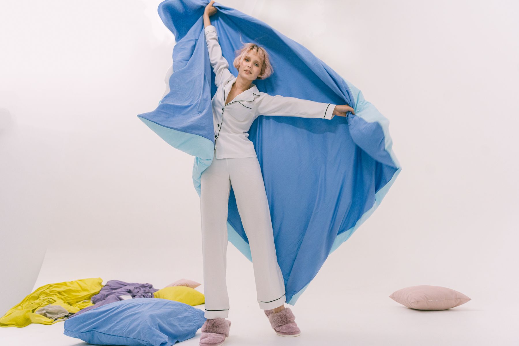 Model in a pajama set holding up a length of pale blue fabric in a studio