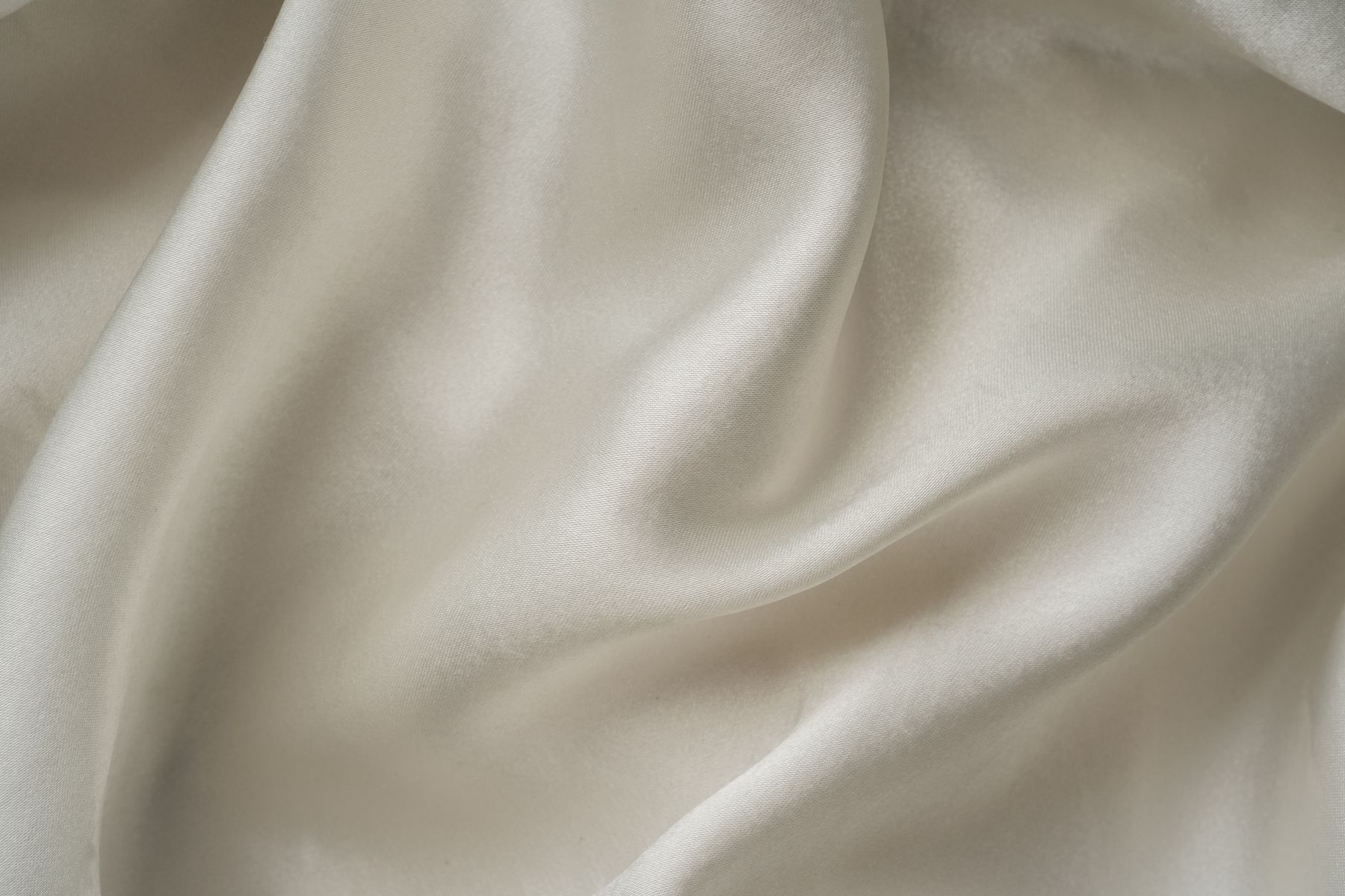 Close-up of ivory fabric falling in soft folds, showing a fluid silky drape