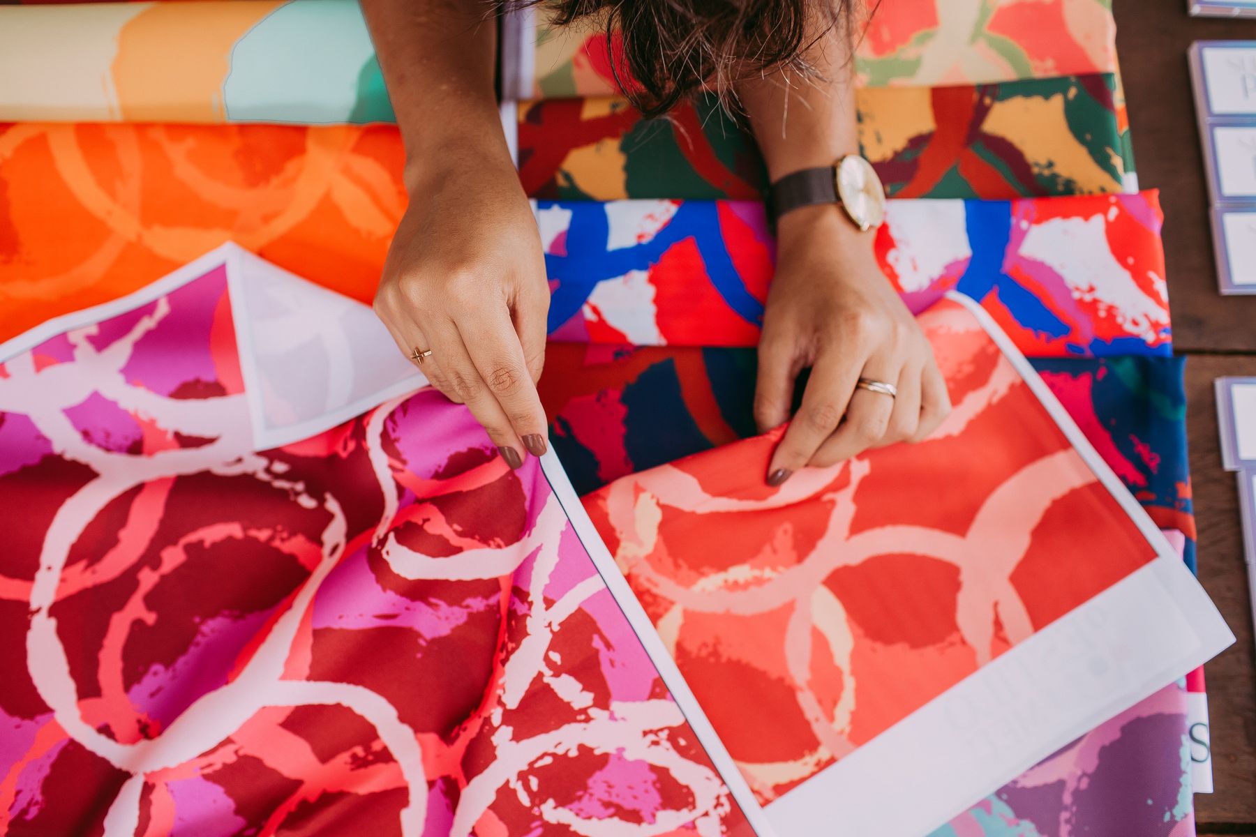 Hands comparing printed fabric colourways laid out on a table