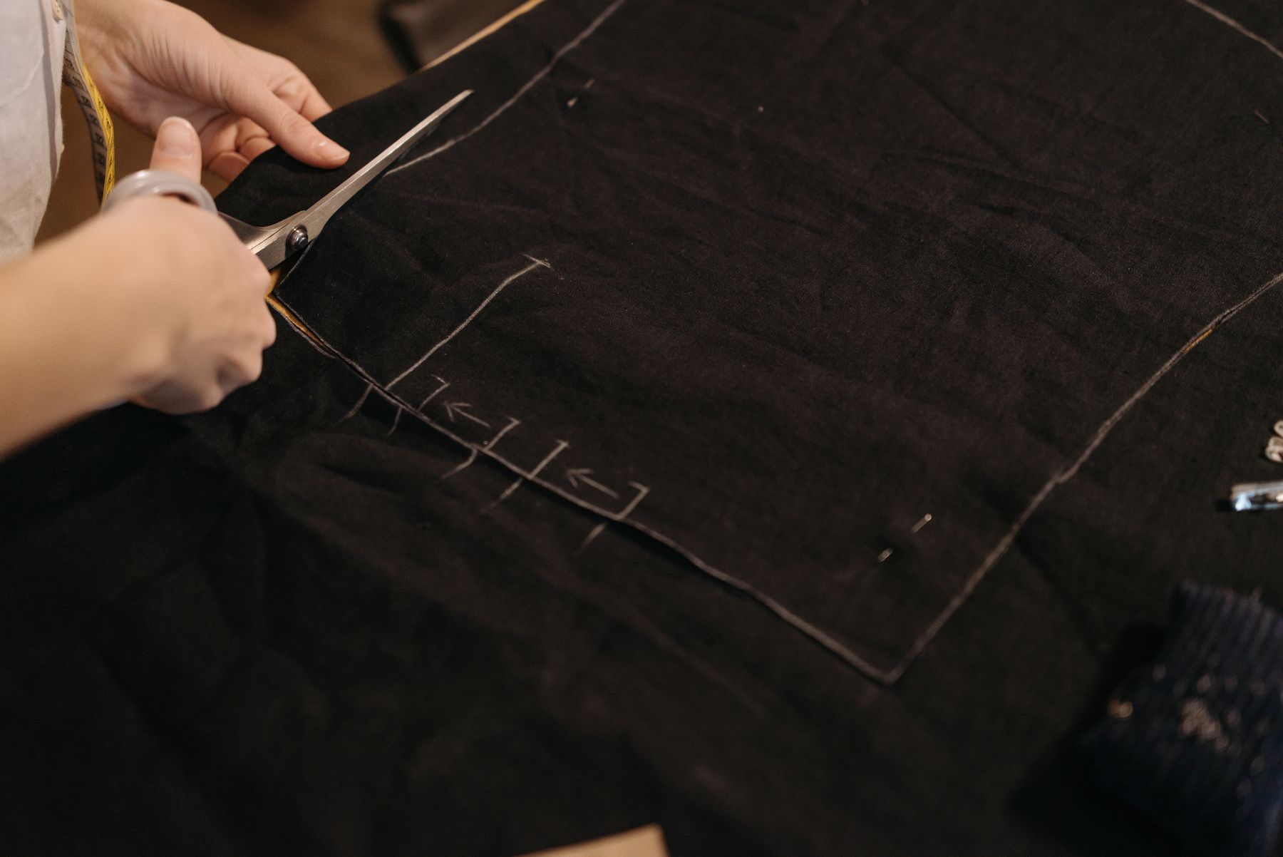 Hands cutting dark fabric along a marked line