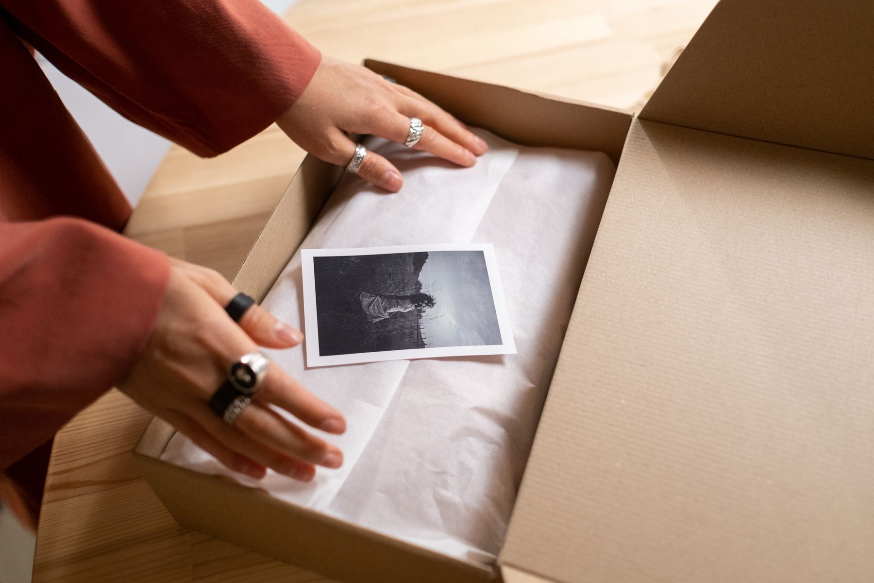 Hands packing a garment into a box between sheets of tissue paper