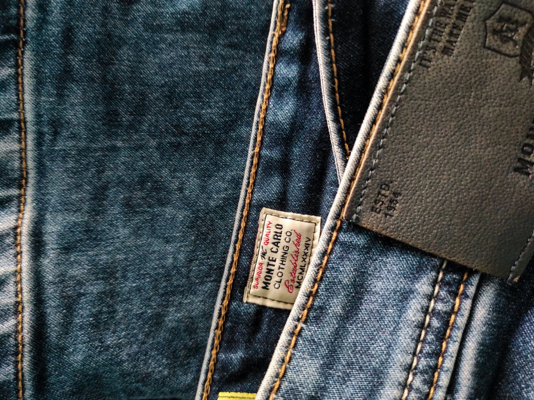 Woven brand label and leather patch stitched onto a denim garment