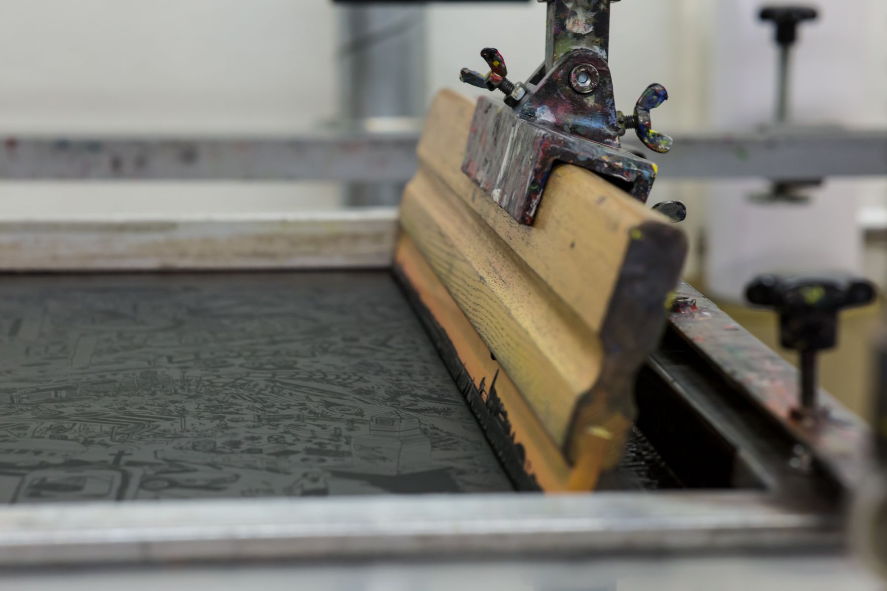 Screen printing press with a squeegee resting on the print screen