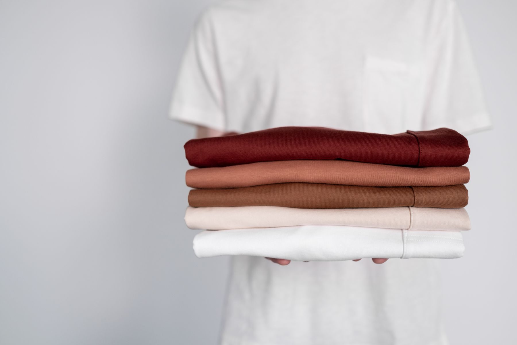 Person holding a stack of neatly folded garments in earthy tones