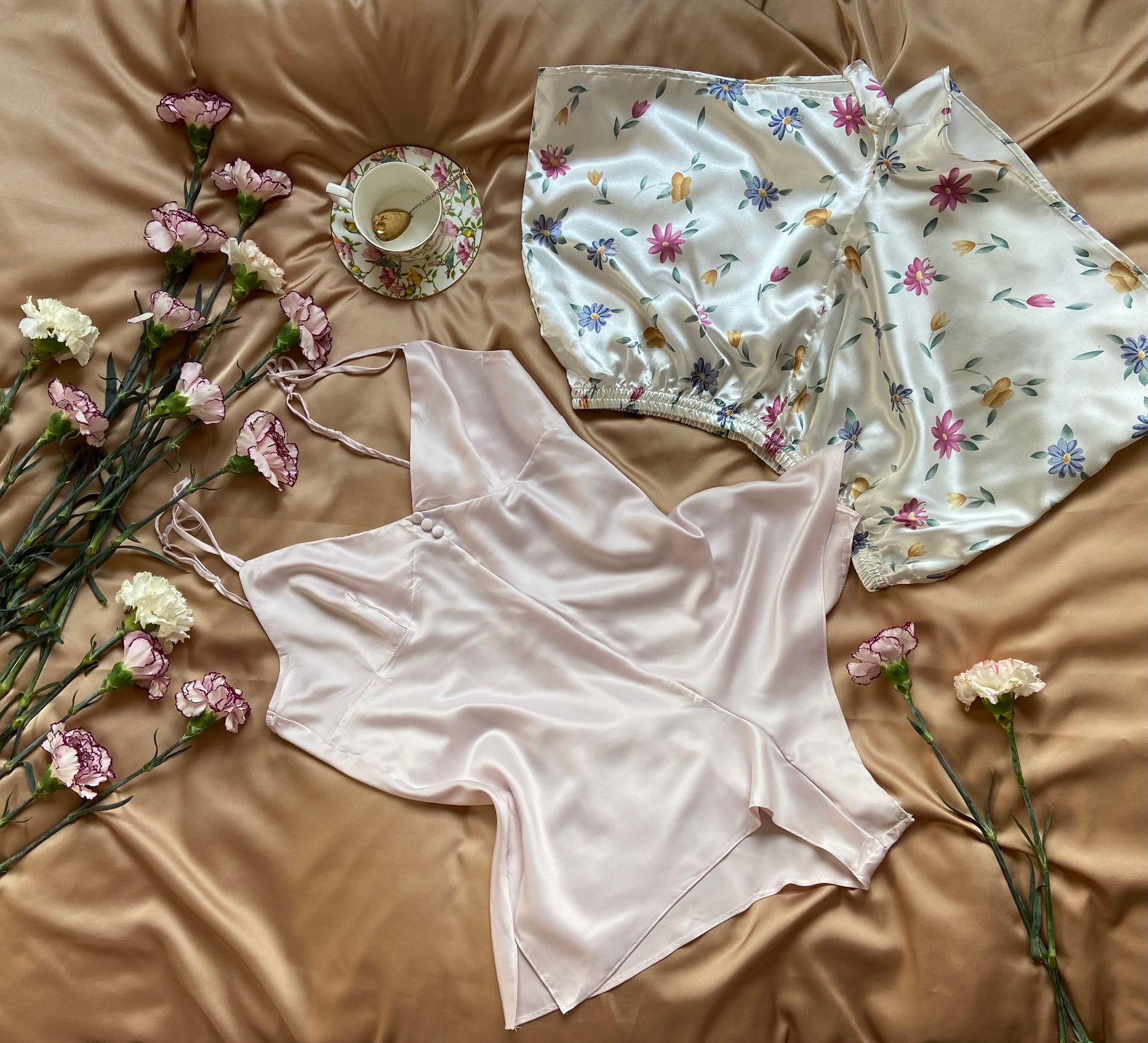 Floral pajama set and satin camisole laid out flat with a teacup and flowers
