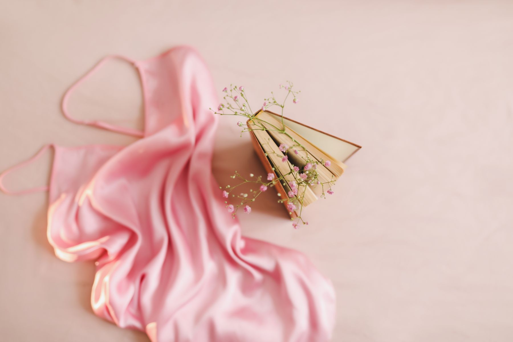 Pink satin nightdress arranged on a pale background beside a book