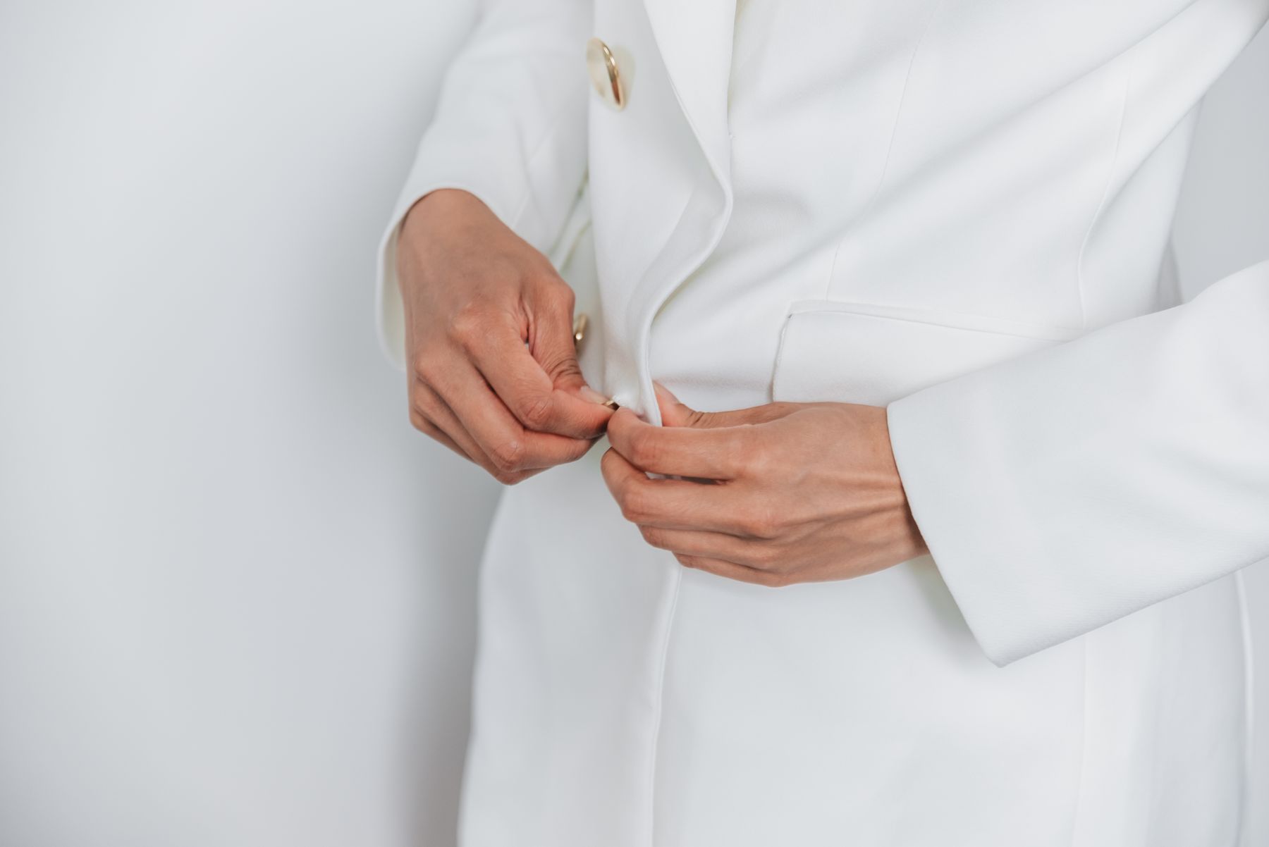 Hands fastening a button on a white garment